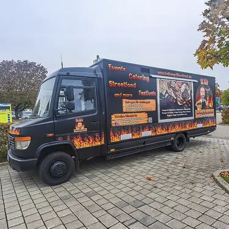 Fahrzeugbeschriftung für Balkangrill Foodtruck (SAM): schwarzer Foodtruck mit Flammen-Design, „Events, Catering, Streetfood“ und Website.